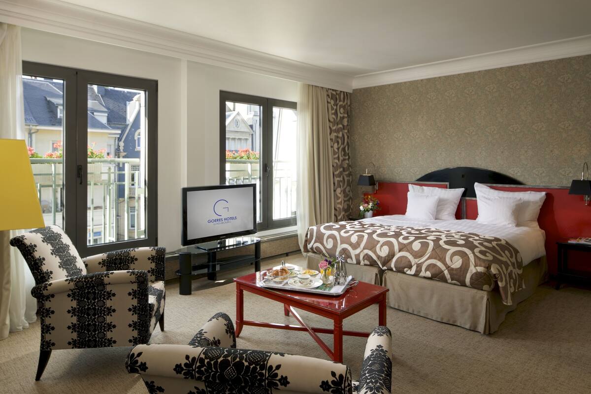 Een hotelkamer met een bed, een televisie, een koffietafel met ontbijt en uitzicht op een balkon.