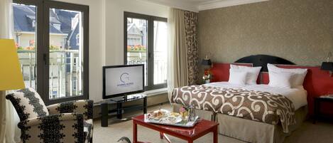 Une chambre d’hôtel avec un lit, une télévision, une table basse avec le petit-déjeuner, et un balcon avec vue.