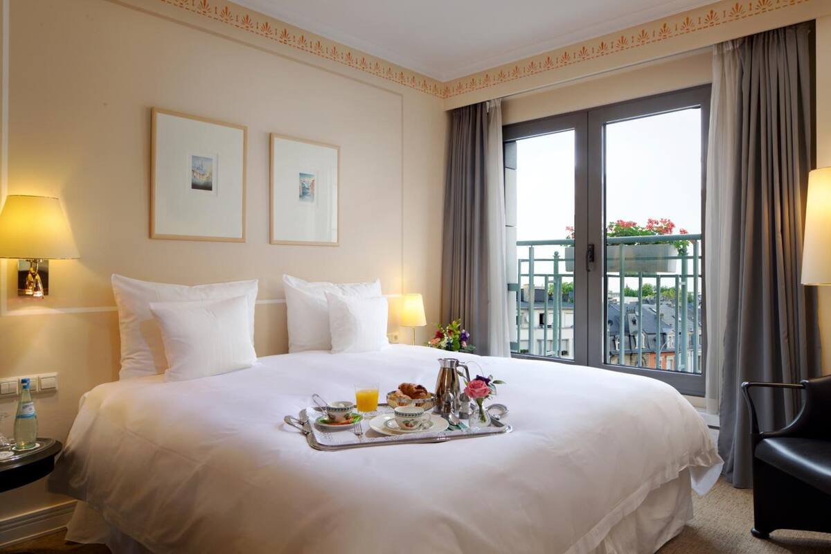 Een hotelkamer met een groot bed, een dienblad met ontbijtartikelen, een balkon met uitzicht en een stoel.