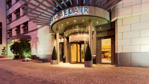Exterior de l'Hotel Belair, amb un disseny modern, que destaca per una entrada corba i una señalització il·luminada.
