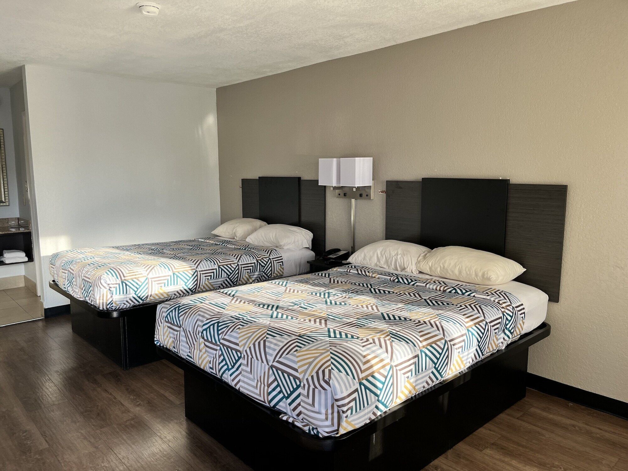 Una habitació d'hotel amb dos llits, cadascun amb un estovat estampat i una làmpada de nit.