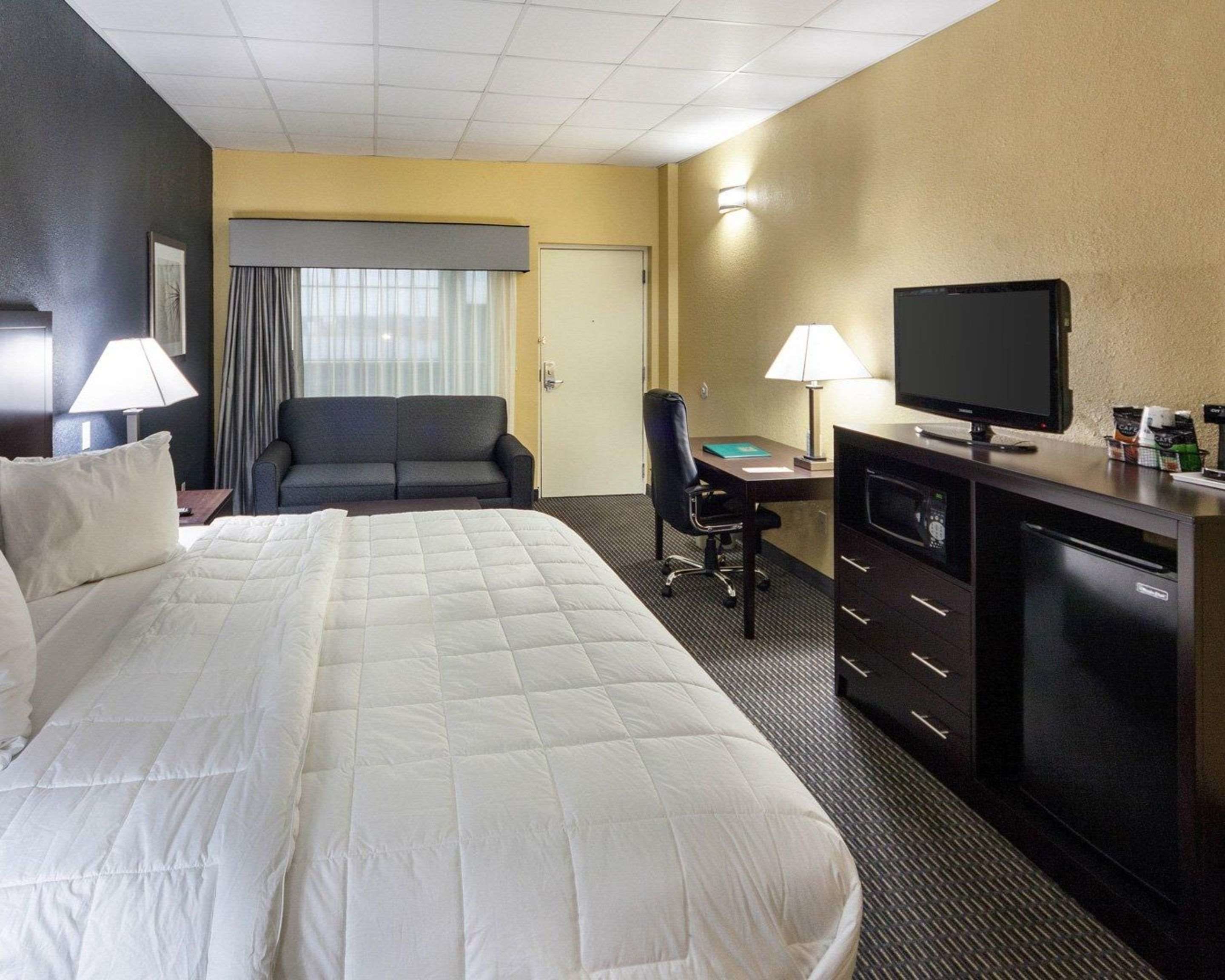 Een hotelkamer met een groot bed, een bureau met een televisie, een stoel en een bureaulamp.
