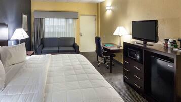 Een hotelkamer met een groot bed, een bureau met een televisie, een stoel en een bureaulamp.