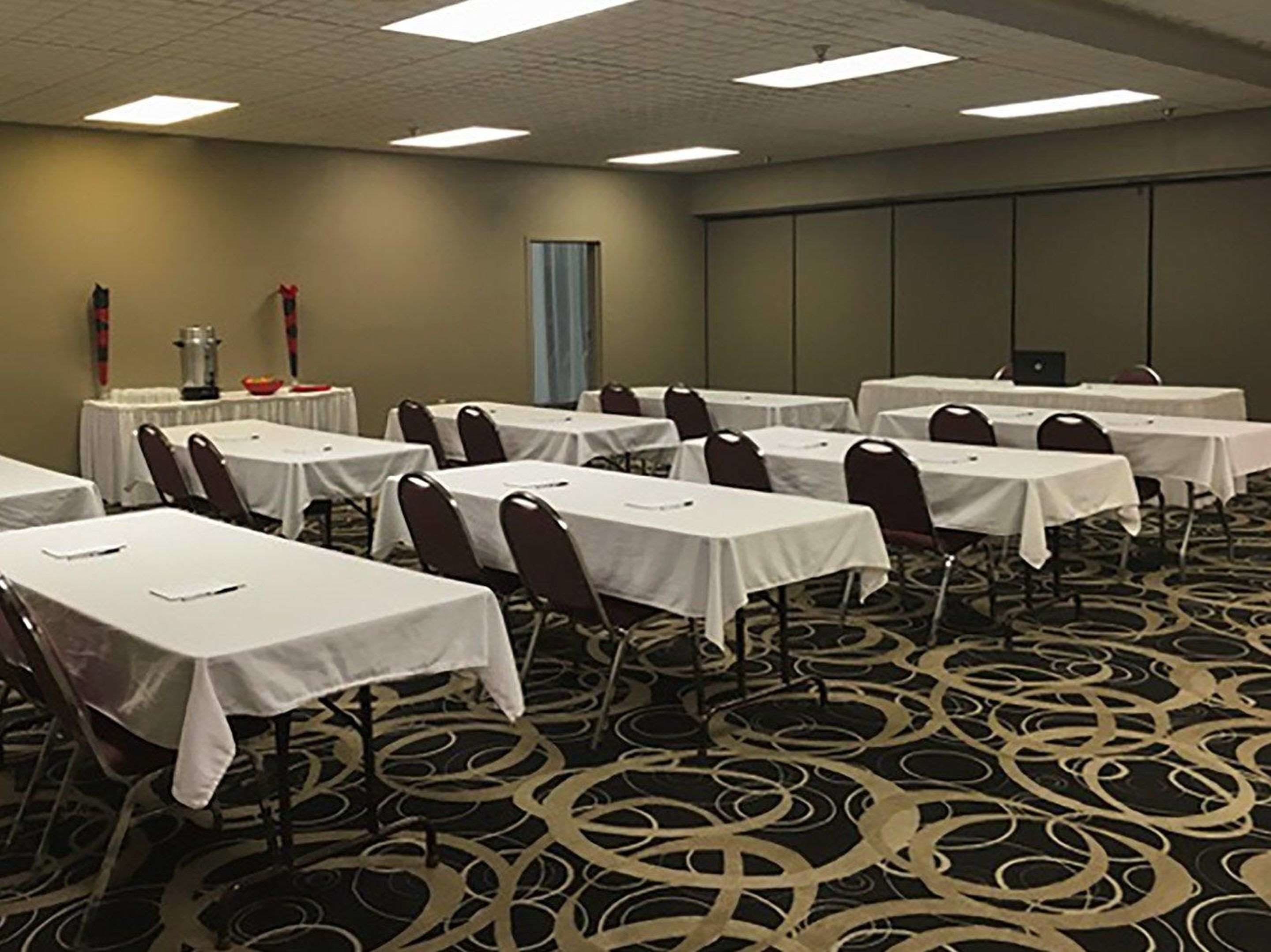 A conference room with multiple tables and chairs, a carpeted floor, and a plain wall with a door.