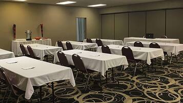A conference room with multiple tables and chairs, a carpeted floor, and a plain wall with a door.