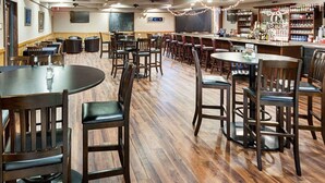 Un restaurant doté de nombreuses tables et chaises, d’un bar bien garni avec une variété de bouteilles et de ventilateurs de plafond.