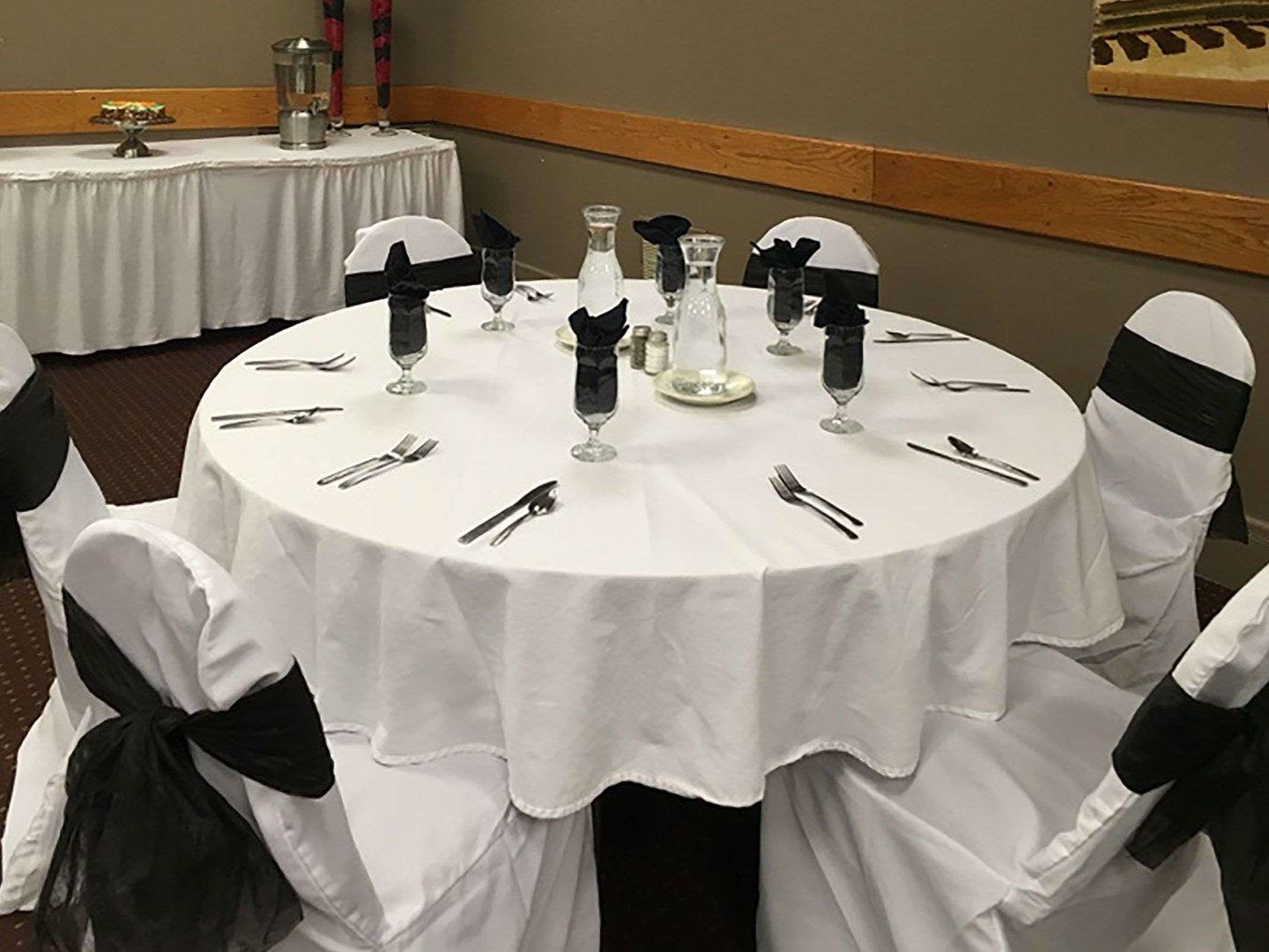 A round dining table with white tablecloth, black napkins, and silverware.