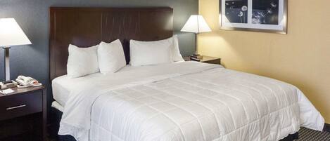 Quarto de hotel com uma cama grande, duas mesas de cabeceira com luminárias, um telefone e um quadro na parede.