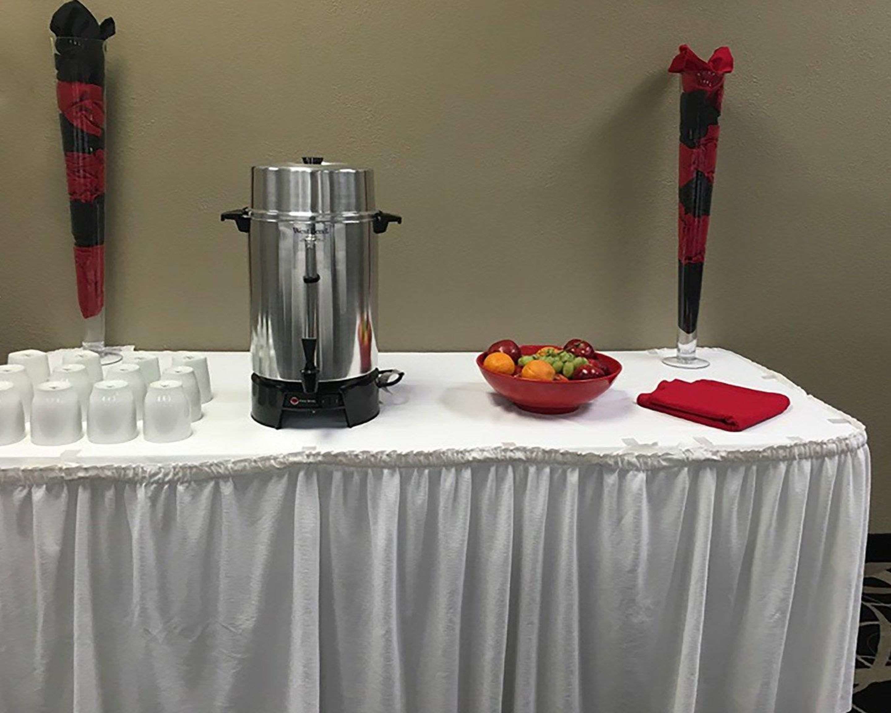 A table with a coffee maker, a bowl of fruit, and several cups.