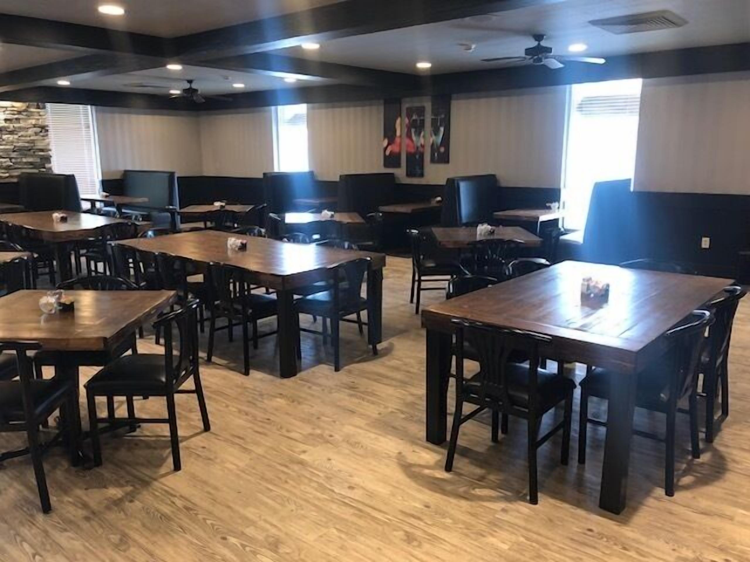 A restaurant with wooden tables and chairs, a stone accent wall, and ceiling fans.