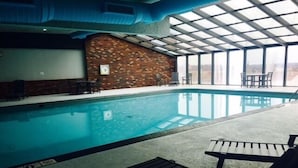 Une piscine intérieure avec un mur en briques, des chaises longues et de grandes fenêtres.