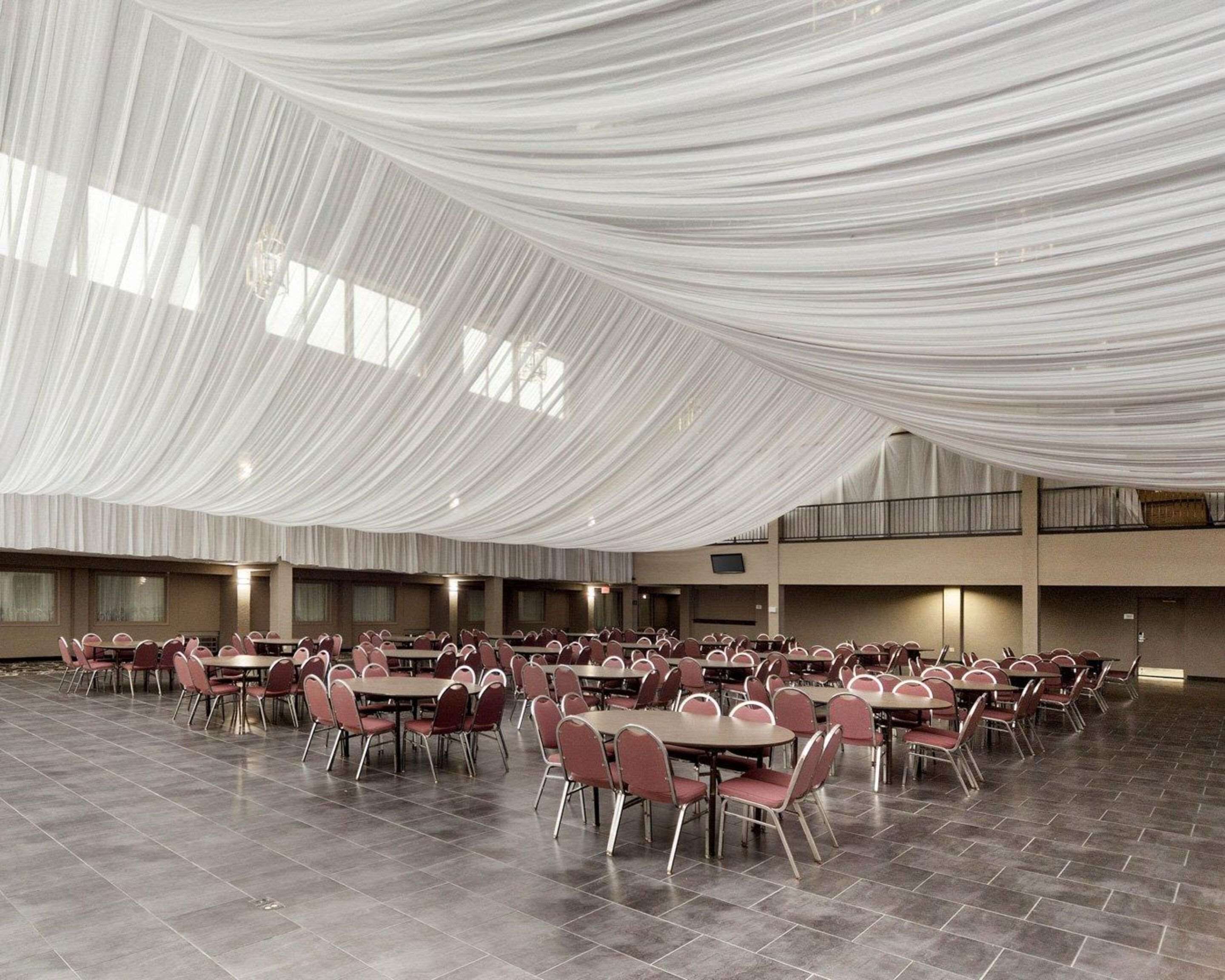 Un salón amplio con filas de mesas y sillas, cubierto con tela blanca.