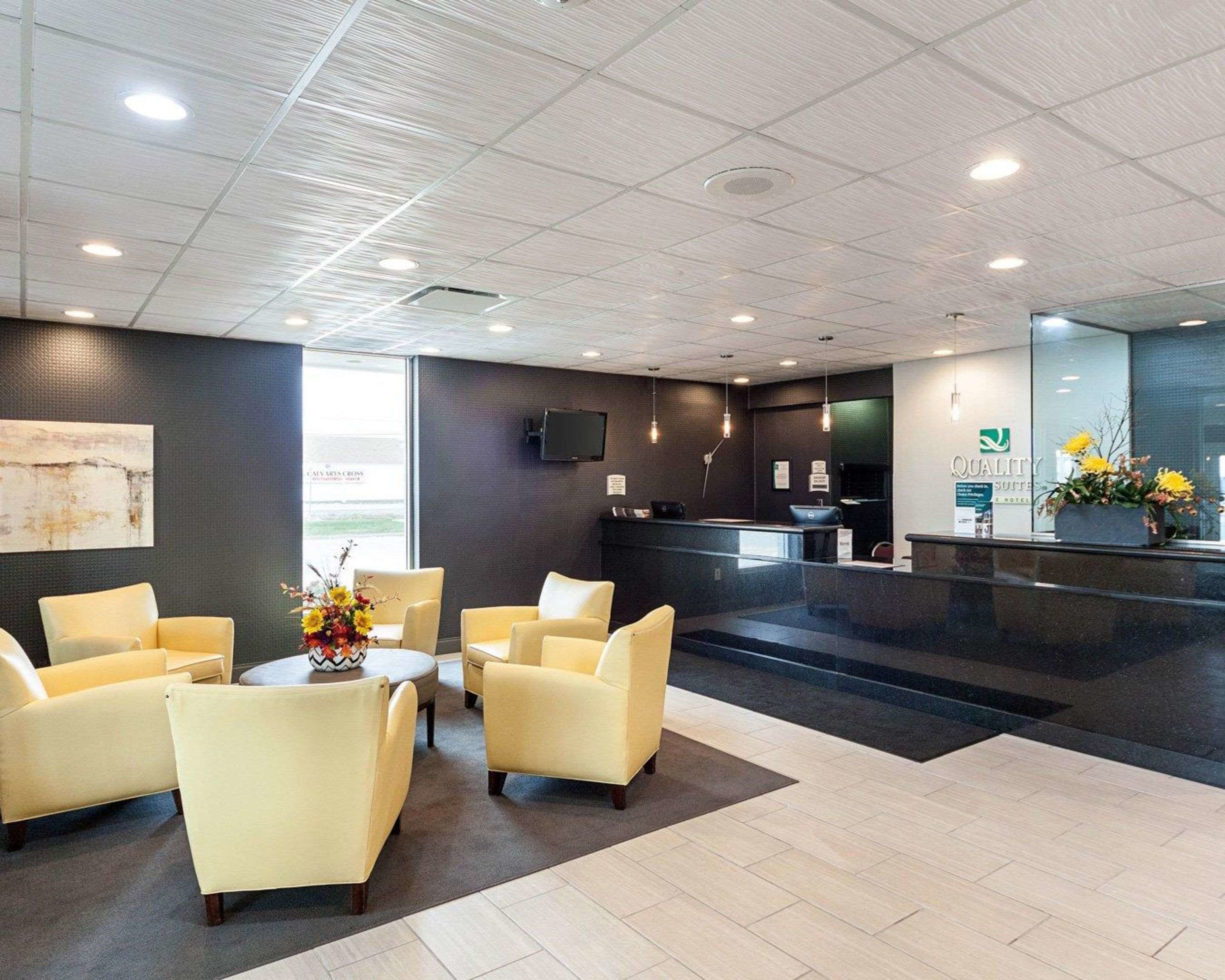 A hotel reception area with a reception desk, a flat-screen TV, and a seating area with chairs and a table.
