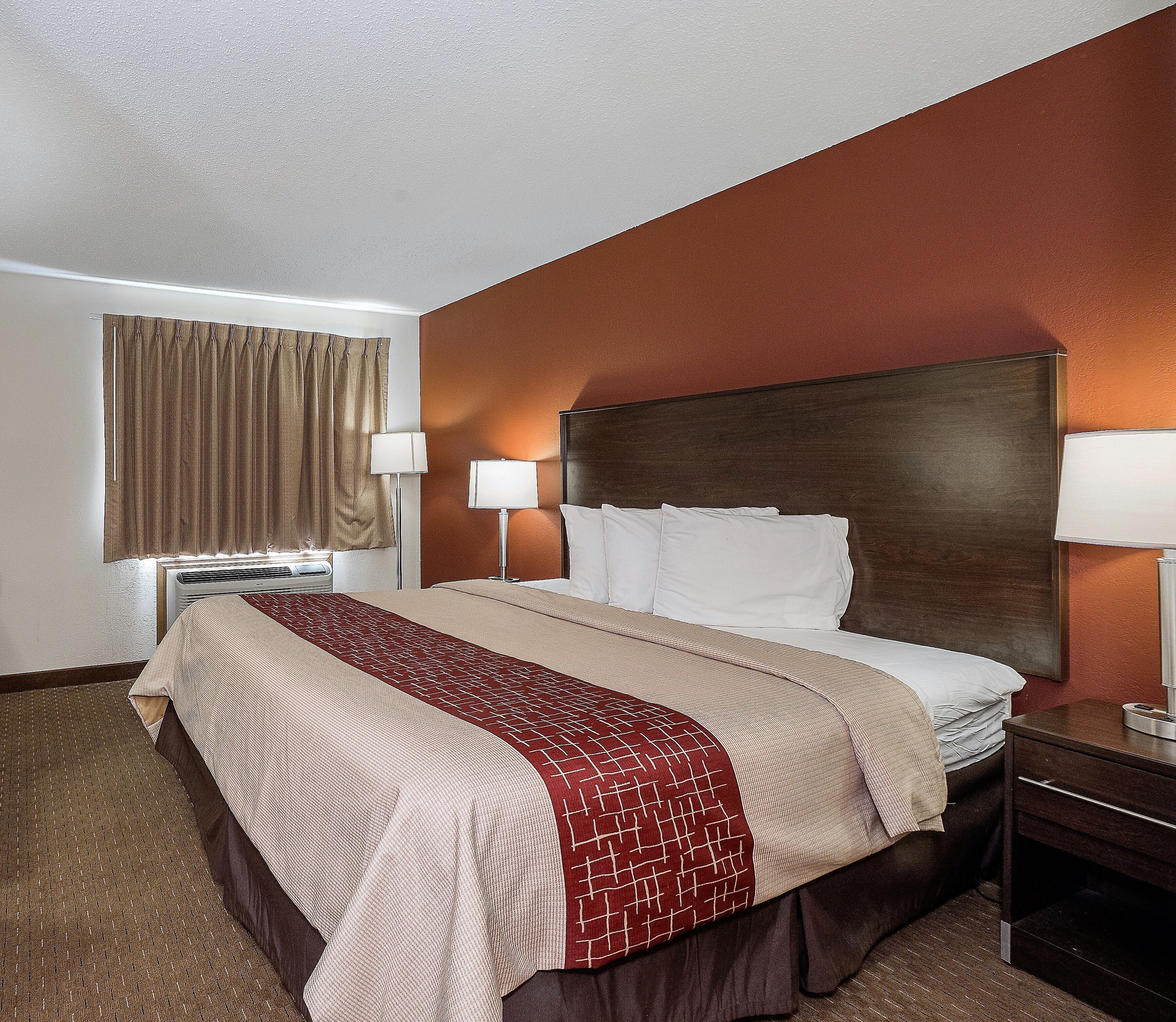 A hotel room with a large bed, two bedside lamps, a window with curtains, and a wooden headboard.