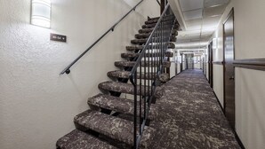 A carpeted staircase with a handrail, a light fixture on the wall, and a directional sign.