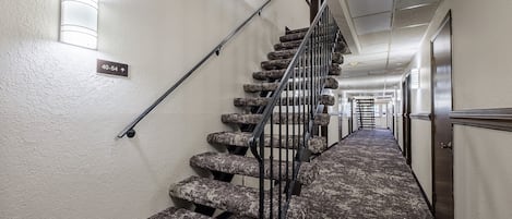 A carpeted staircase with a handrail, a light fixture on the wall, and a directional sign.