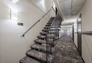 A carpeted staircase with a handrail, a light fixture on the wall, and a directional sign. - Red Roof Inn Dayton - Huber Heights (Dayton)