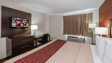 A hotel room with a bed, a desk, a chair, a television, two lamps, and an air conditioning unit.