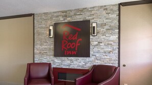 A Red Roof Inn reception area with a stone wall, two leather chairs, and a flat-screen TV.