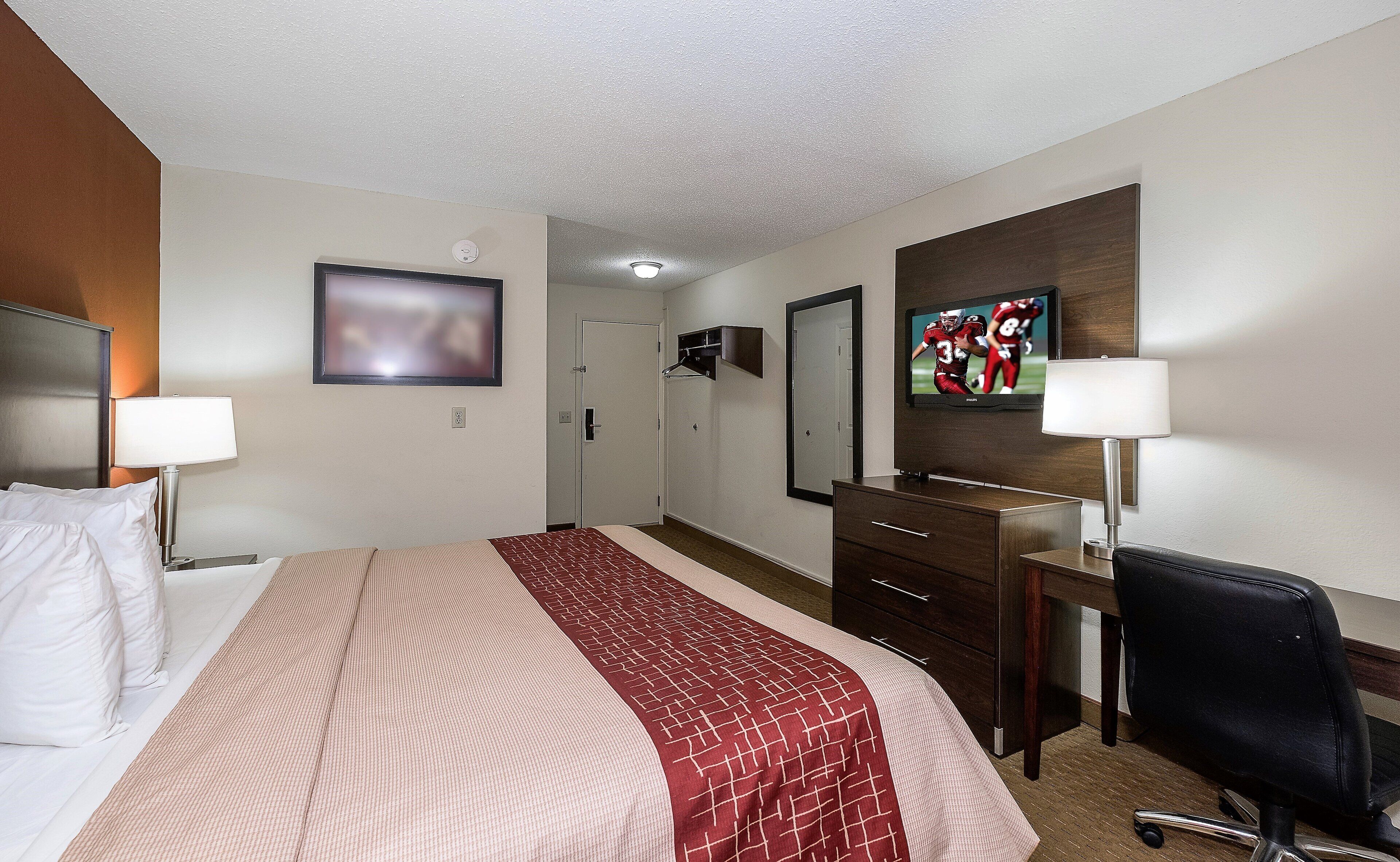 A hotel room with a bed, a desk, a chair, a television, and a mirror.