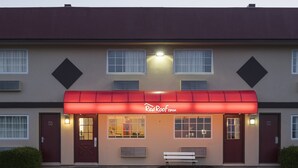 A Red Roof Inn with a red awning, a bench outside, and a parking lot in front.