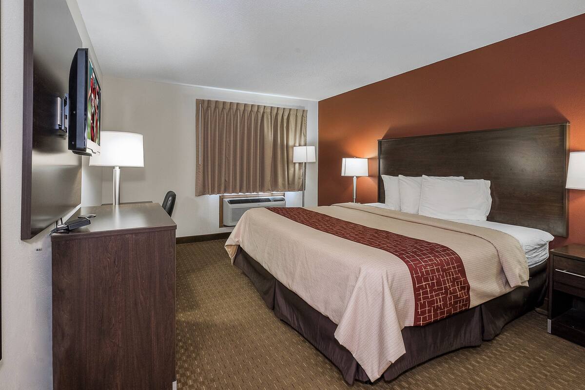 Une chambre d’hôtel dotée d’un grand lit, de lampes de chevet, d’un bureau avec une lampe, d’un téléviseur à écran plat et d’un climatiseur fixé au mur.