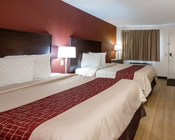 A hotel room with two beds, a nightstand, a lamp, a window with curtains, and a door.