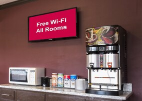 A coffee machine, a microwave, and a television displaying 'Free Wi-Fi All Rooms' in a room with a brown wall.