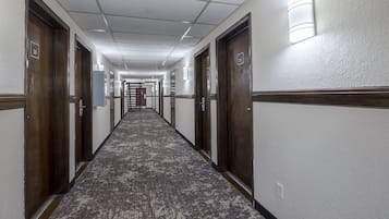 Pasillo de hotel con piso alfombrado, puertas de madera y luminarias fijadas a la pared.