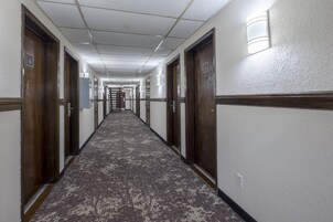 Pasillo de hotel con piso alfombrado, puertas de madera y luminarias fijadas a la pared.