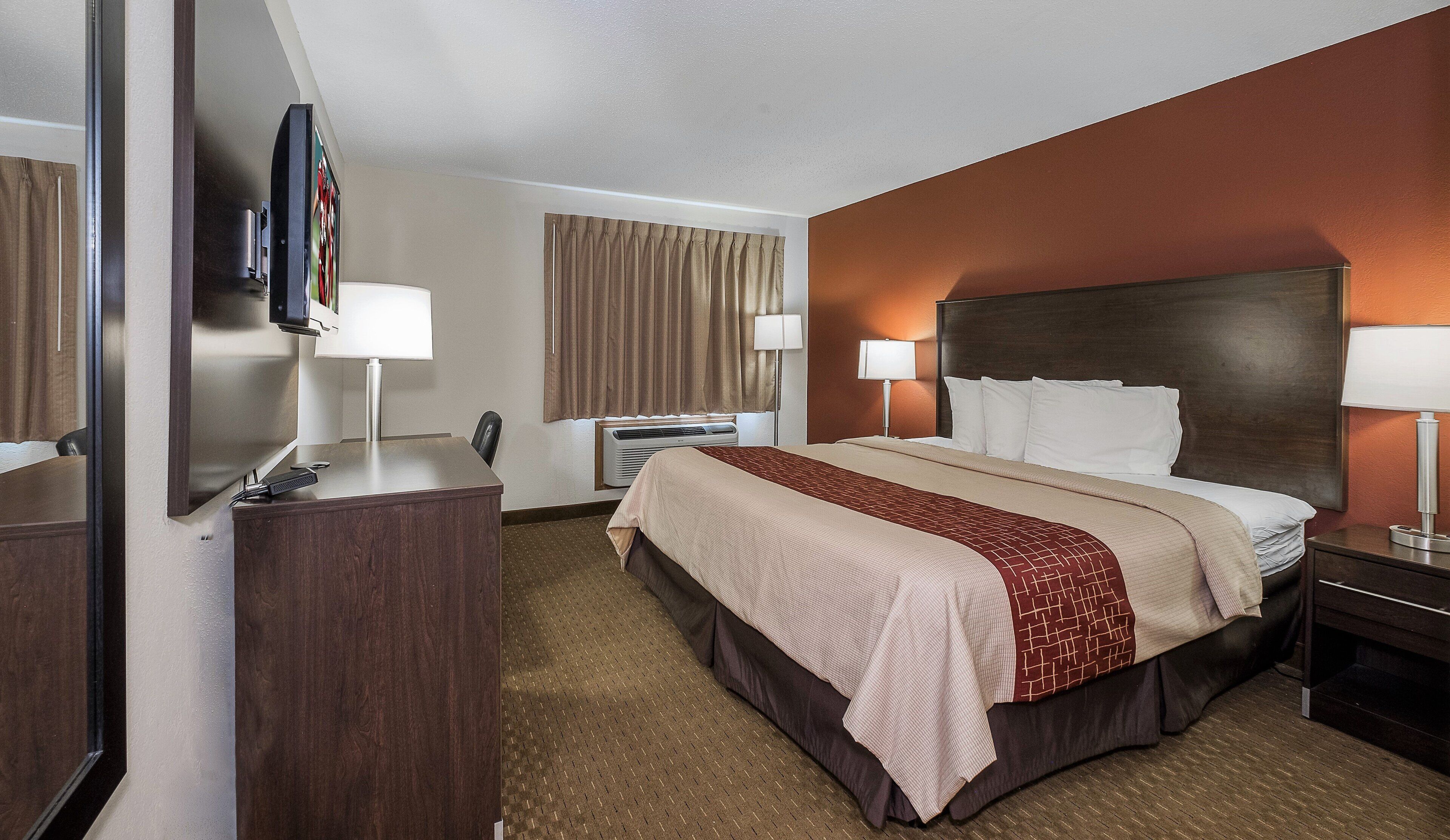 Habitación de hotel con cama, mesitas de noche, escritorio, silla, televisor y ventana con cortinas.