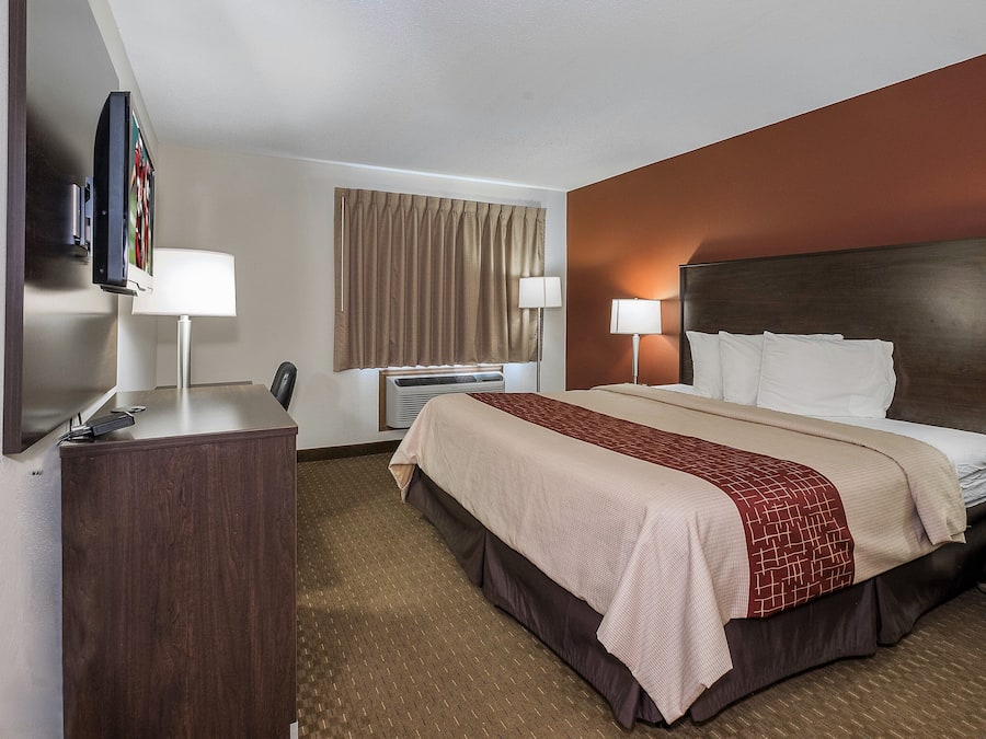 Quarto de hotel com cama, mesas de cabeceira, escrivaninha, cadeira, televisão e janela com cortinas.