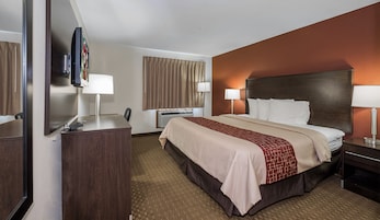 Habitación de hotel con cama, mesitas de noche, escritorio, silla, televisor y ventana con cortinas.