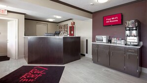 A hotel reception area with a desk, a coffee machine, and a sign indicating free Wi-Fi in all rooms. - Red Roof Inn Dayton - Huber Heights (Dayton)