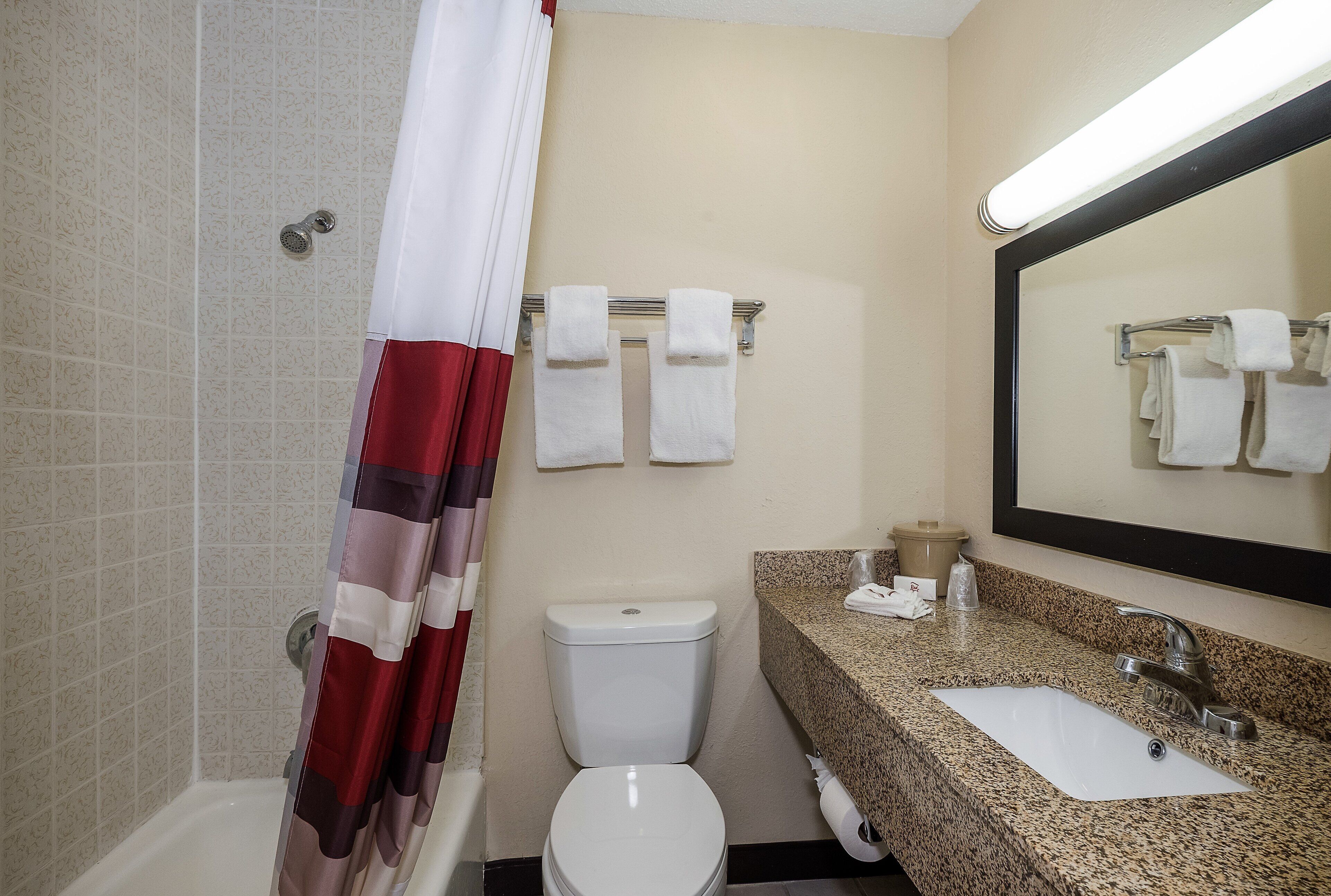 Un baño con inodoro, lavamanos, espejo, toallero y cortina de ducha.