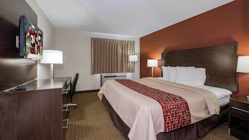 Habitación de hotel con cama, lámparas de noche, un escritorio con silla, televisión y ventana con cortinas.