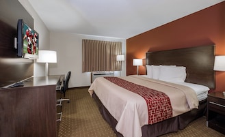 Habitación de hotel con cama, lámparas de noche, un escritorio con silla, televisión y ventana con cortinas.