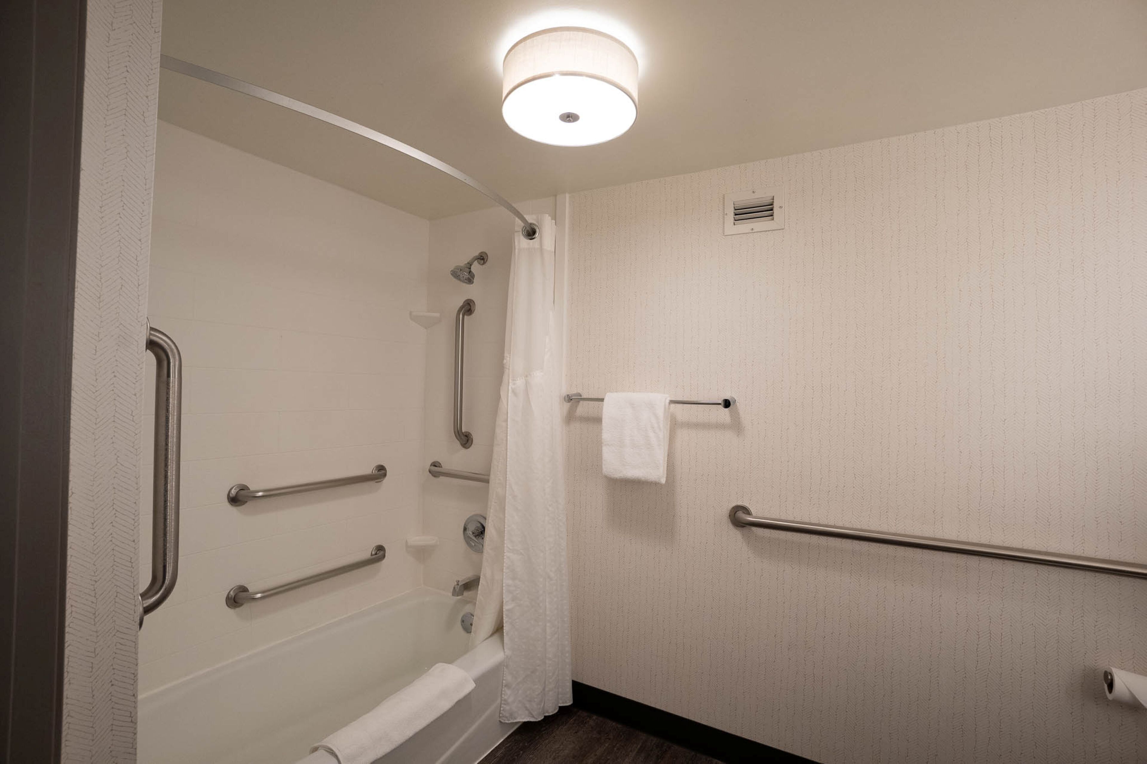 A bathroom with a bathtub, grab bars, a towel rack, and a shower curtain.