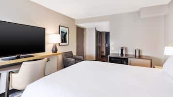 A hotel room with a large bed, a desk with a flat-screen TV, a chair, a coffee maker, and a lamp.