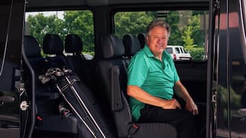 A man seated in a van with luggage and golf clubs in the back.