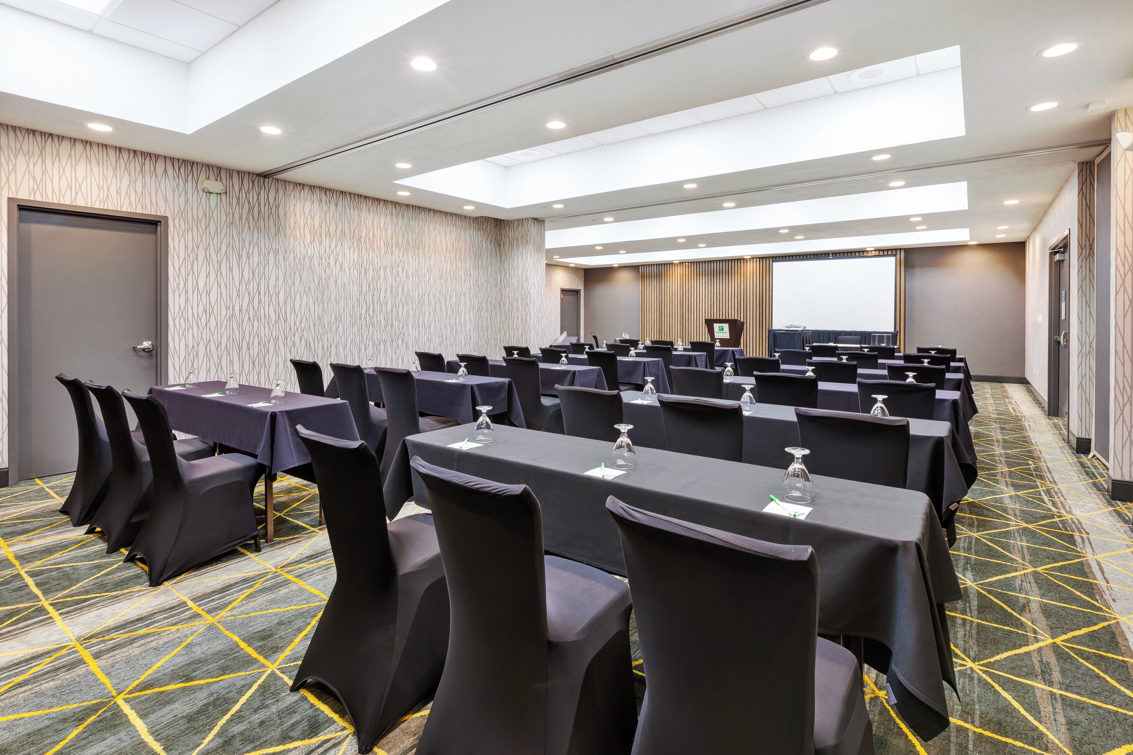A conference room with rows of tables, chairs, and a projection screen.