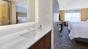 A hotel room with a bathroom, a bed, a desk, and a large window.
