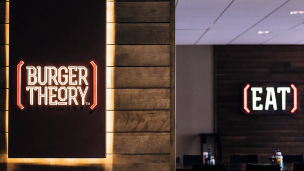 A restaurant interior with a neon sign reading "BURGER THEORY" and another sign saying "EAT".