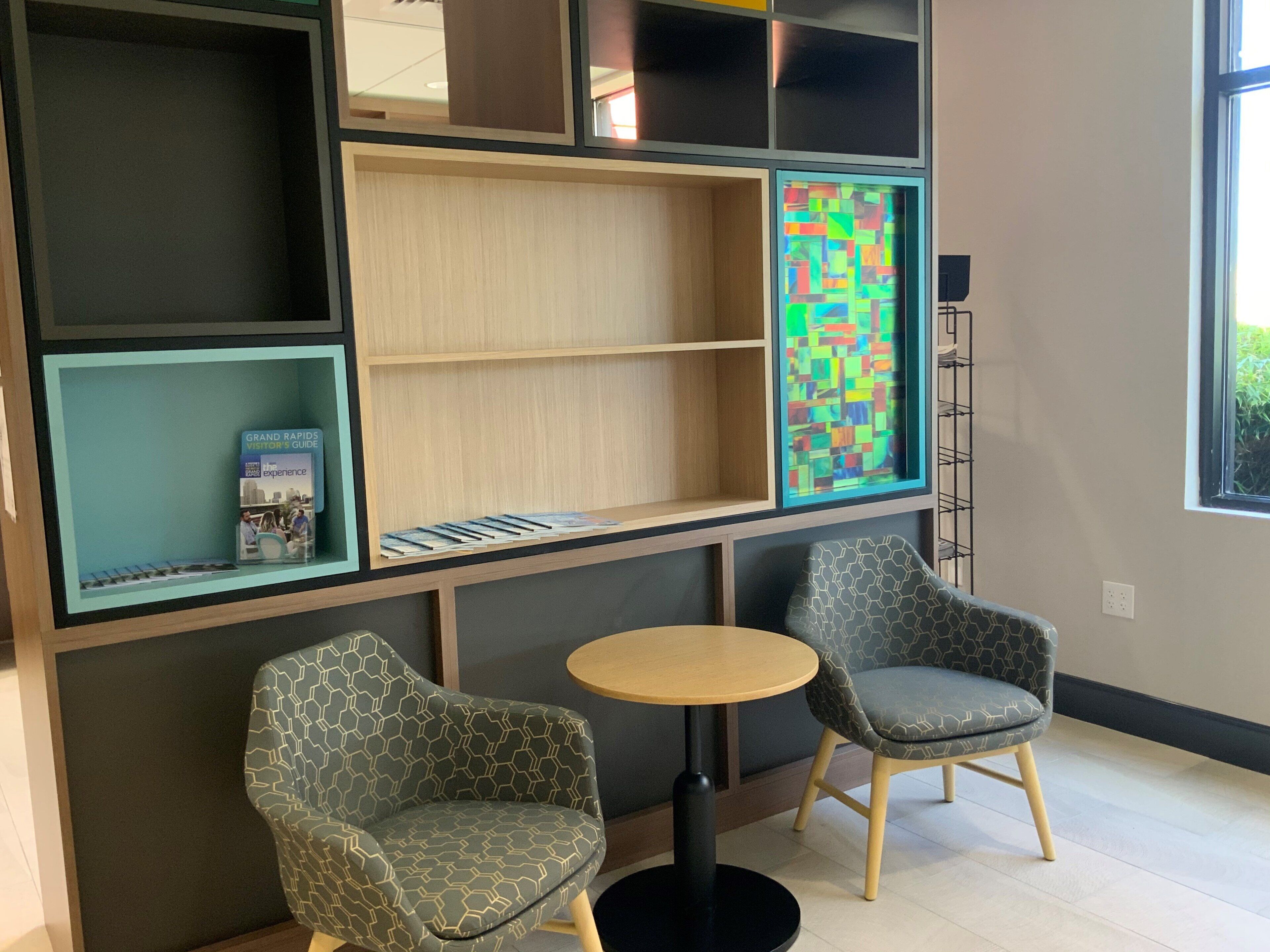 A modern interior with two patterned armchairs, a small round table, and a bookshelf with a colorful abstract artwork.