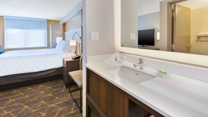 A hotel room with a bed, a bathroom with a sink and mirror, and a television.