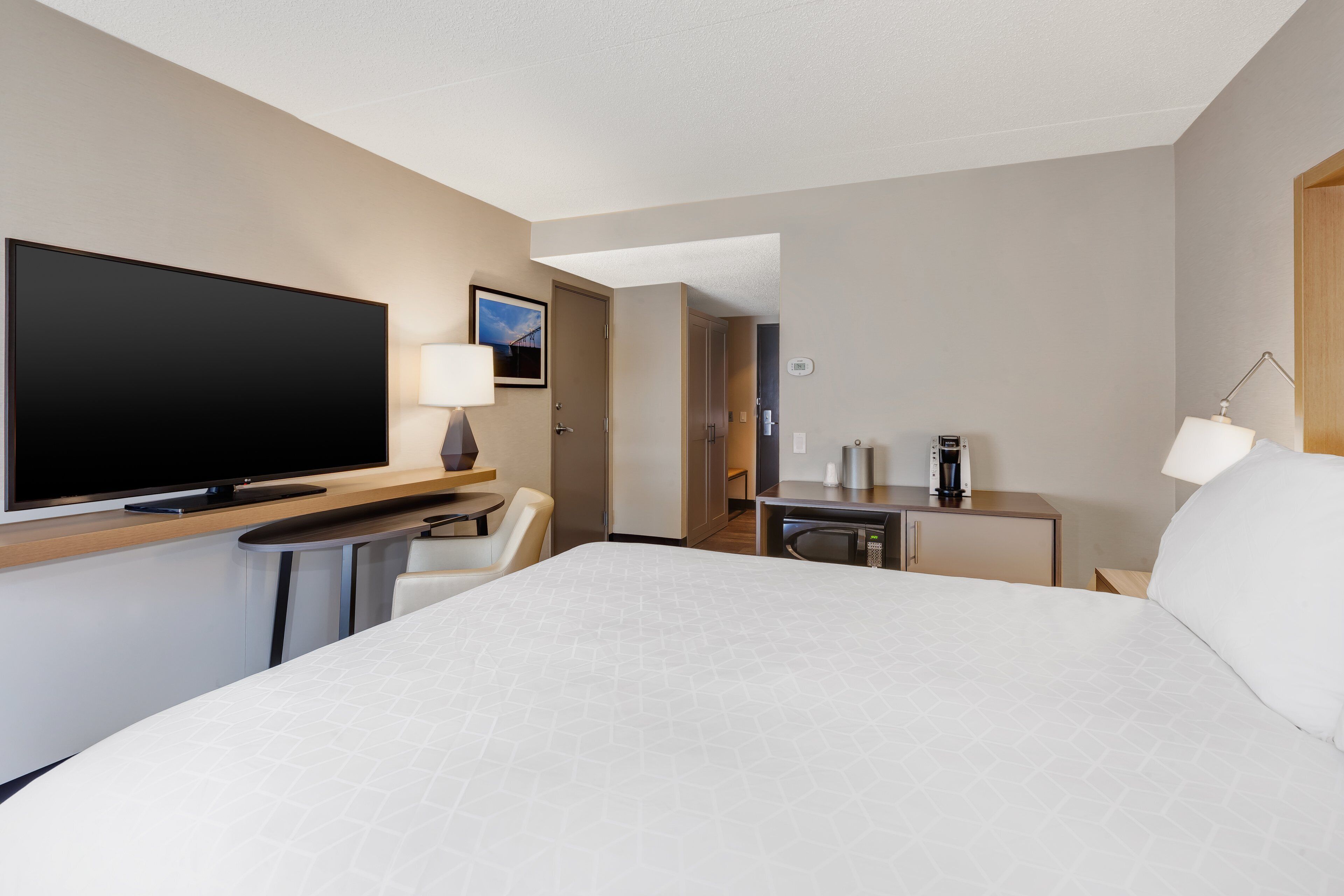 A hotel room with a large bed, a flat-screen TV, a desk with a lamp, and a coffee maker.