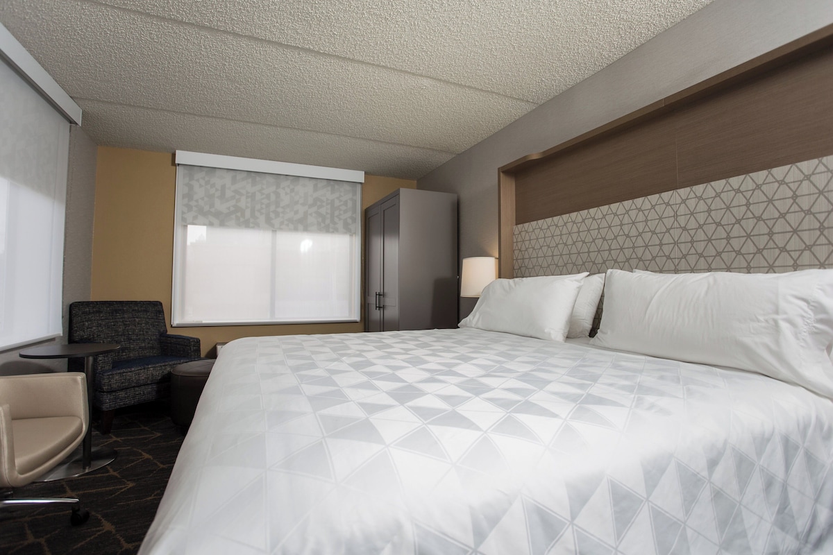 Ein Hotelzimmer mit einem großen Bett, einem Schreibtisch, einem Stuhl, einem Kleiderschrank und einem Fenster mit Vorhängen.