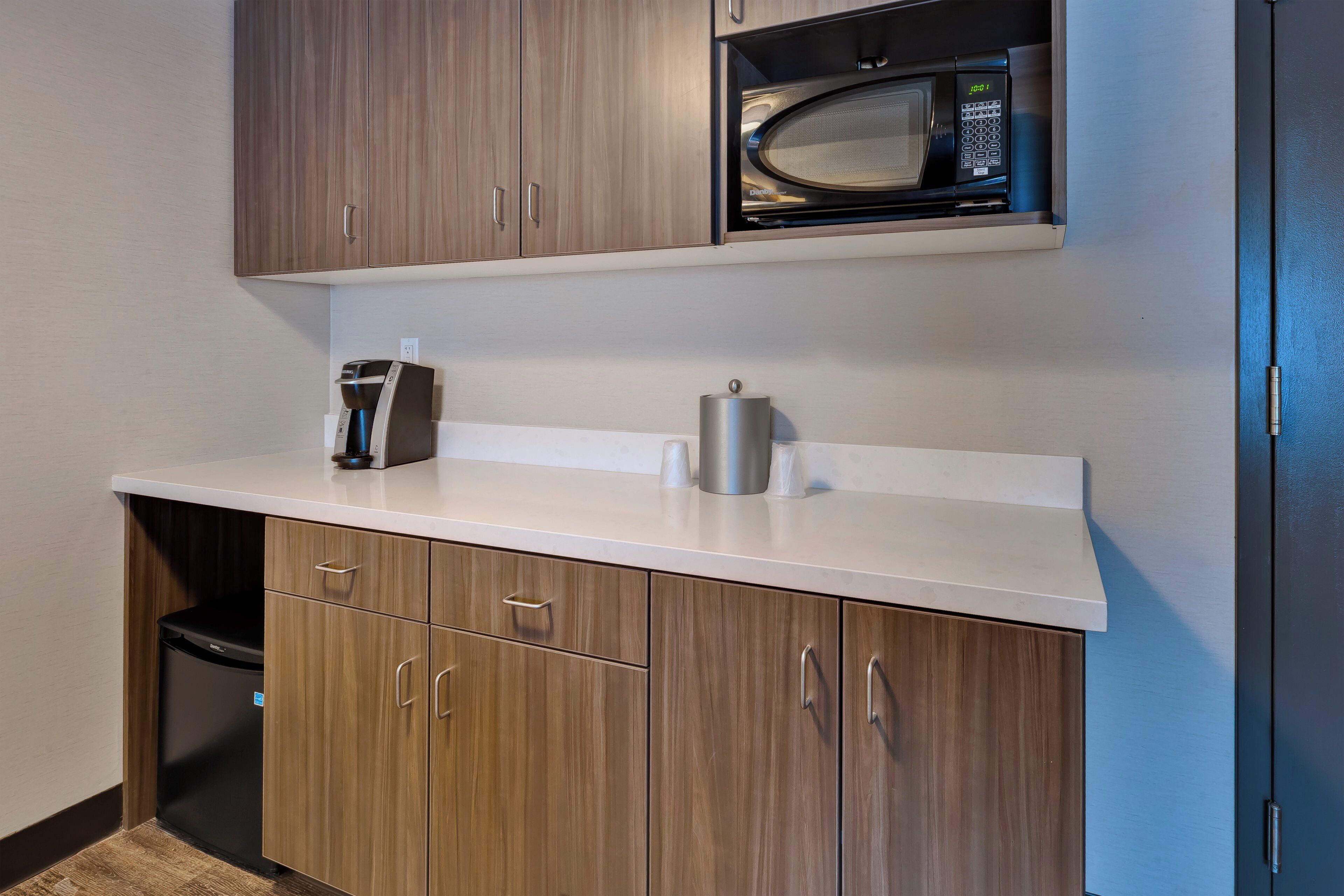 Una kitchenette con microondas, cafetera y un recipiente de acero inoxidable.