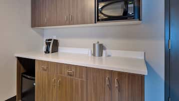 Una kitchenette con microondas, cafetera y un recipiente de acero inoxidable.