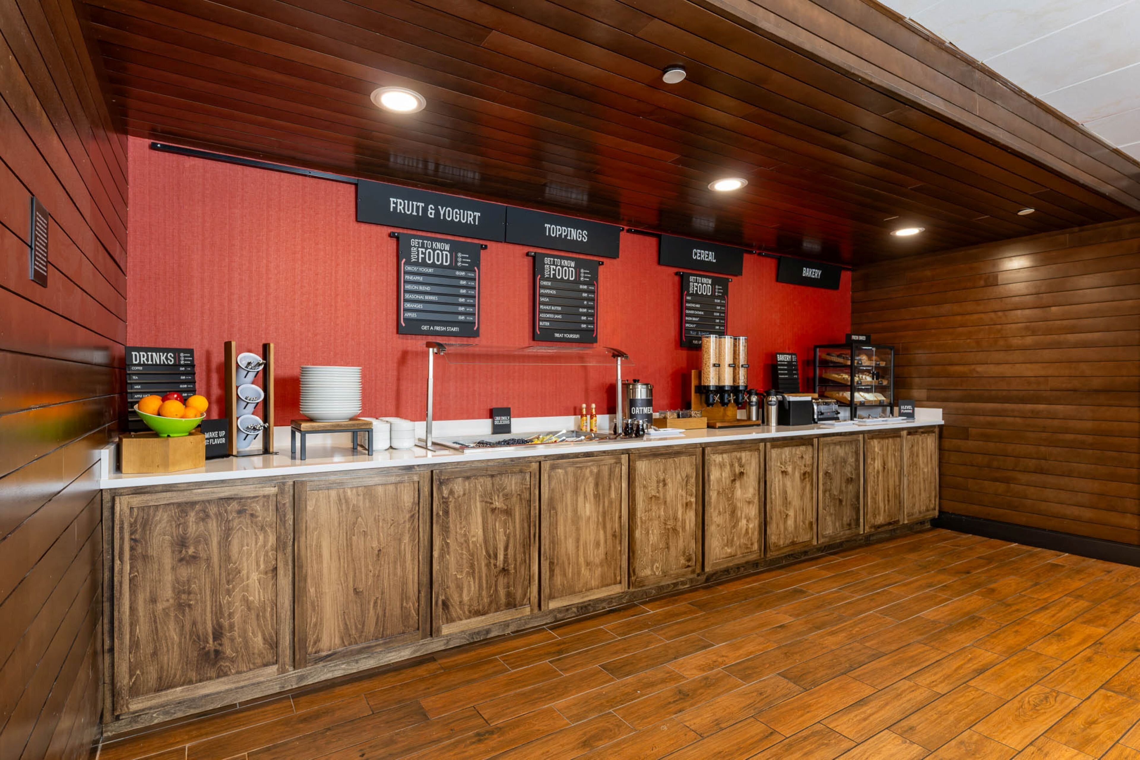 A breakfast bar with wooden cabinets, a red wall, and menu boards for food and drinks.
